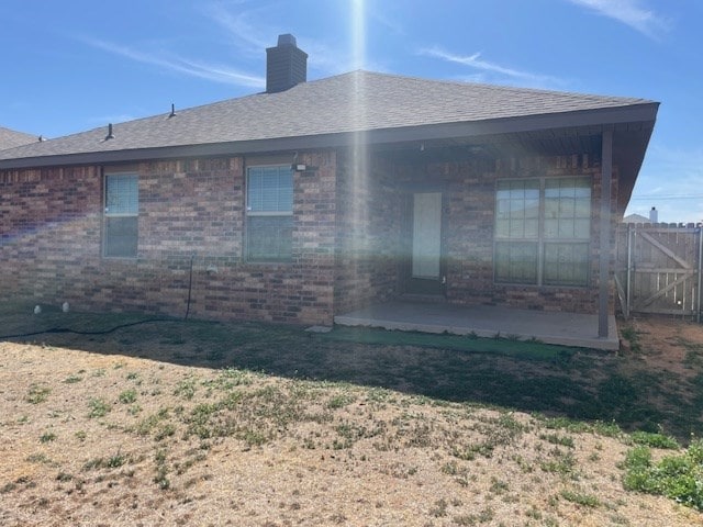 back of property featuring brick siding, a patio, a chimney, a shingled roof, and fence