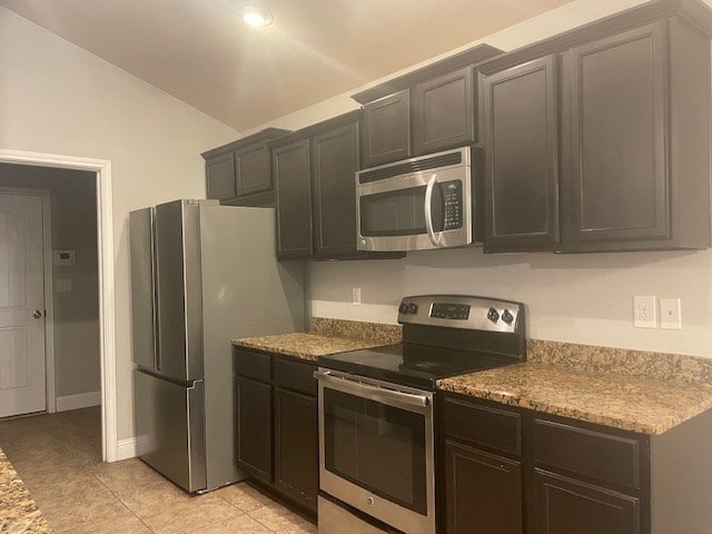 kitchen featuring light tile patterned flooring, stone countertops, stainless steel appliances, baseboards, and vaulted ceiling