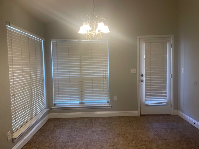 unfurnished dining area featuring tile patterned flooring, baseboards, and an inviting chandelier