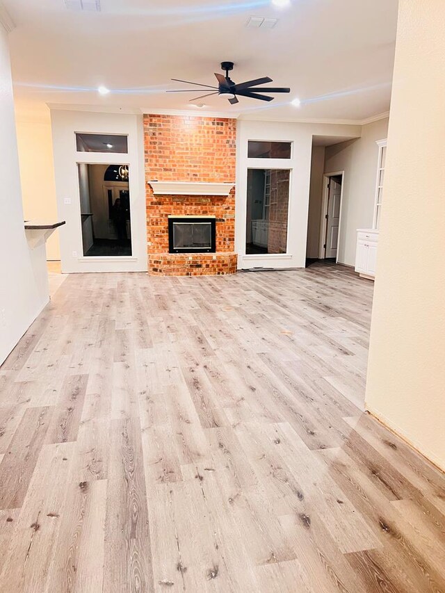 unfurnished living room with ceiling fan, crown molding, a fireplace, and light hardwood / wood-style flooring