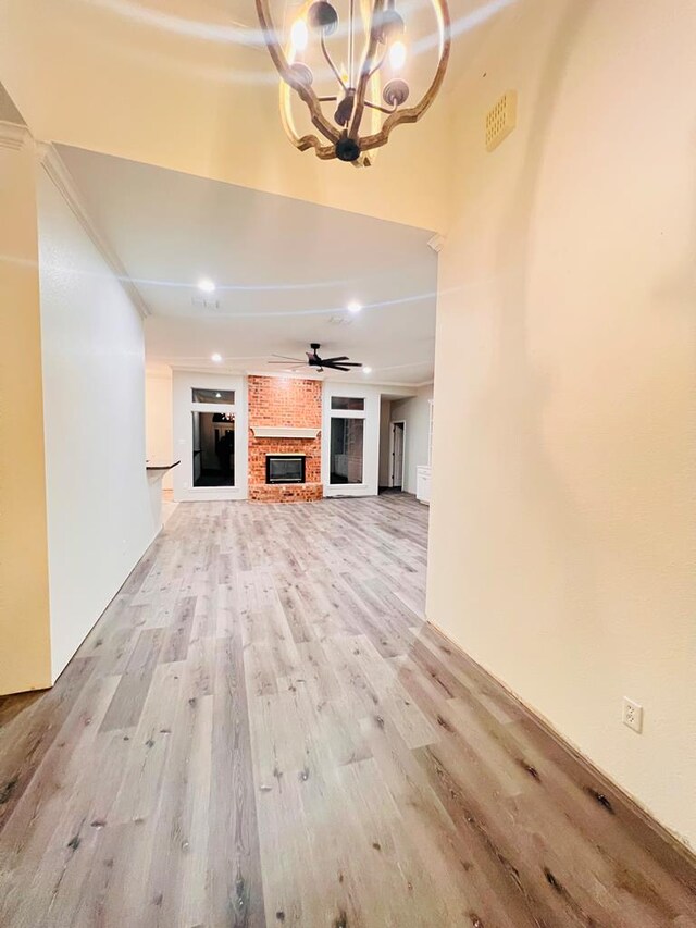 unfurnished living room featuring crown molding, a fireplace, light hardwood / wood-style floors, and ceiling fan with notable chandelier