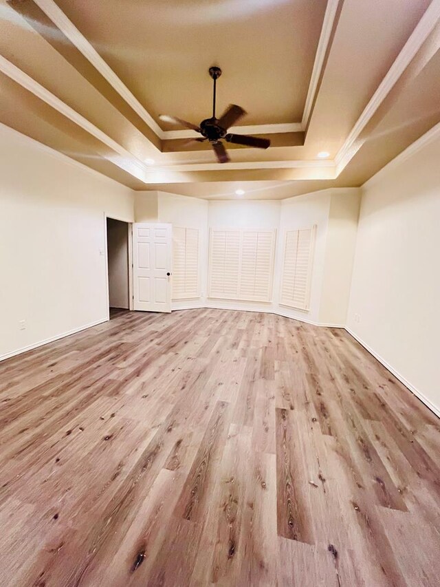 unfurnished room with light wood-type flooring, a tray ceiling, ceiling fan, and ornamental molding