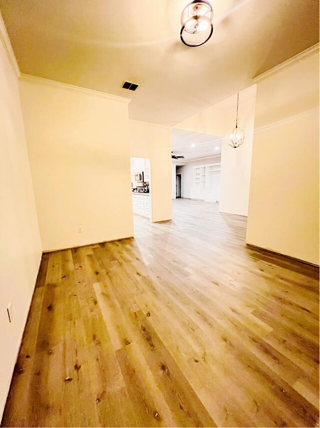 empty room with crown molding, a notable chandelier, and hardwood / wood-style flooring