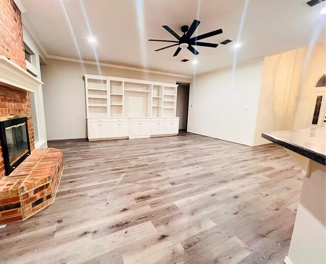 unfurnished living room featuring ceiling fan, light hardwood / wood-style floors, ornamental molding, and a fireplace