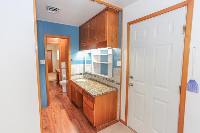 kitchen with tasteful backsplash, light stone countertops, sink, and hardwood / wood-style floors