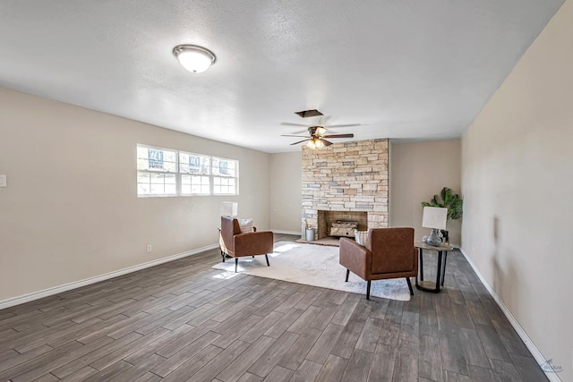 sitting room featuring baseboards, visible vents, a ceiling fan, dark wood-style flooring, and a stone fireplace