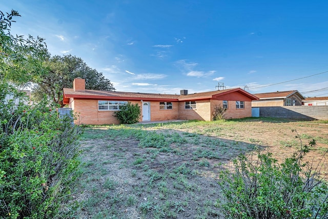 back of house featuring brick siding, a lawn, a chimney, and fence