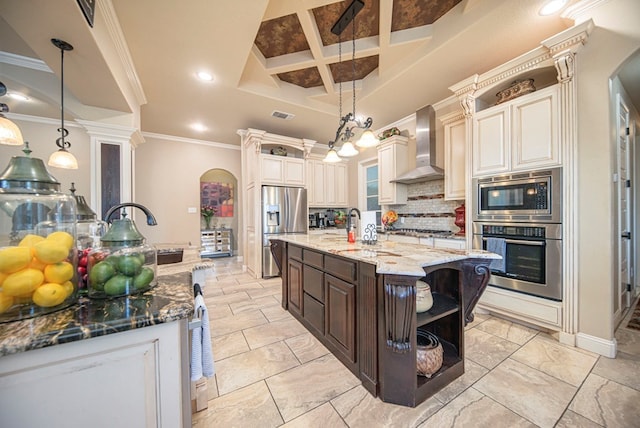 kitchen featuring pendant lighting, coffered ceiling, a center island with sink, wall chimney exhaust hood, and stainless steel appliances