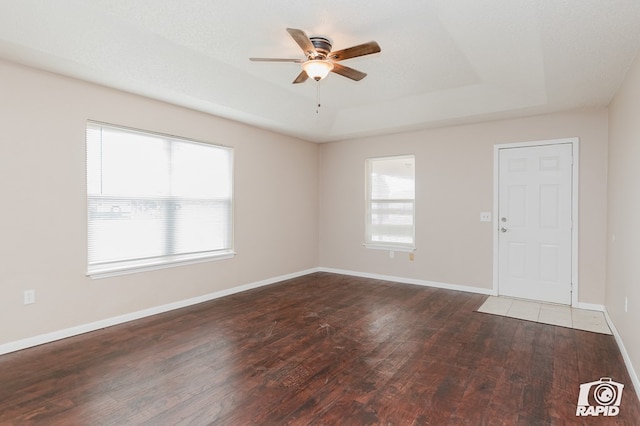 empty room with a textured ceiling, a tray ceiling, ceiling fan, and dark wood-type flooring