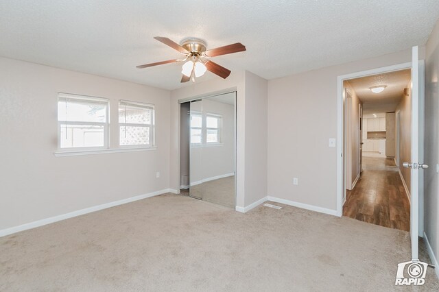 unfurnished bedroom featuring light carpet, a textured ceiling, a closet, and ceiling fan