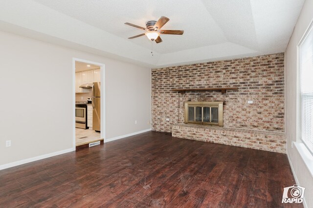 unfurnished living room with a brick fireplace, brick wall, a tray ceiling, ceiling fan, and hardwood / wood-style floors