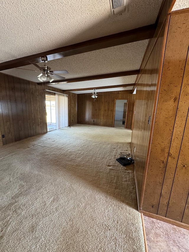 interior space featuring a textured ceiling, carpet, beamed ceiling, and wood walls