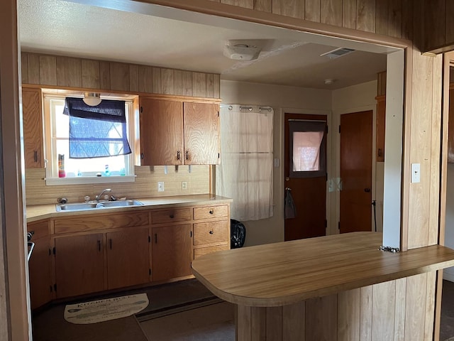 kitchen featuring kitchen peninsula, decorative backsplash, sink, and wood walls