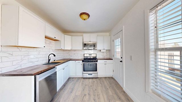 kitchen with butcher block counters, decorative backsplash, white cabinetry, appliances with stainless steel finishes, and sink