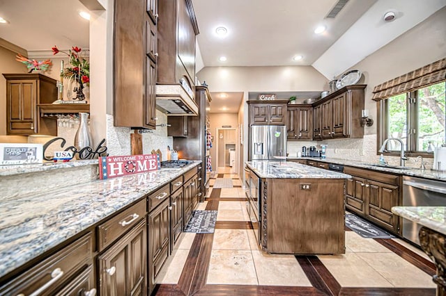 kitchen with light stone countertops, stainless steel appliances, sink, a center island, and lofted ceiling