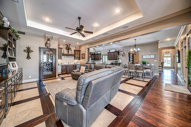 living room with a tray ceiling, crown molding, ceiling fan with notable chandelier, and light wood-type flooring