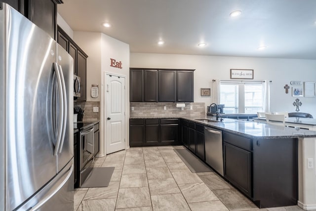 kitchen featuring a sink, decorative backsplash, stone counters, a peninsula, and appliances with stainless steel finishes