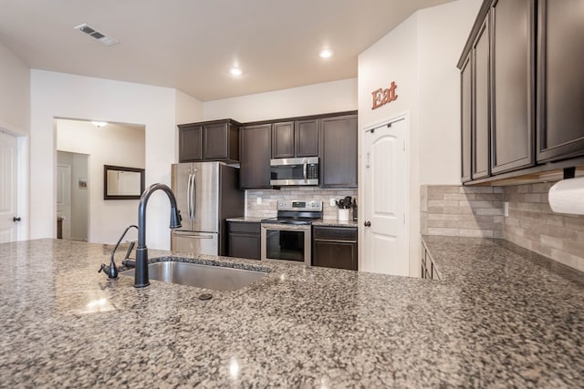 kitchen featuring dark stone counters, stainless steel appliances, dark brown cabinets, a sink, and visible vents