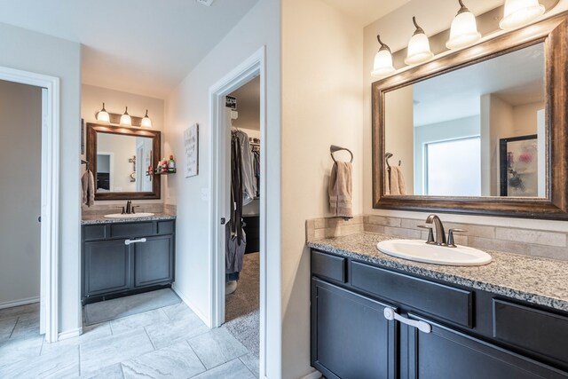 full bathroom featuring two vanities, a walk in closet, baseboards, and a sink