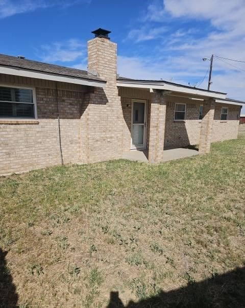 1204 Boykin Rd, Big Spring, TX 79720 - back of property with a chimney, brick siding, a yard, and a patio