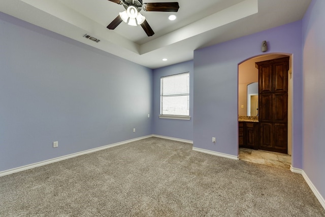 empty room with a tray ceiling, ceiling fan, and light colored carpet