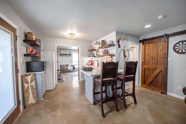 kitchen featuring open shelves, finished concrete floors, freestanding refrigerator, a barn door, and light countertops