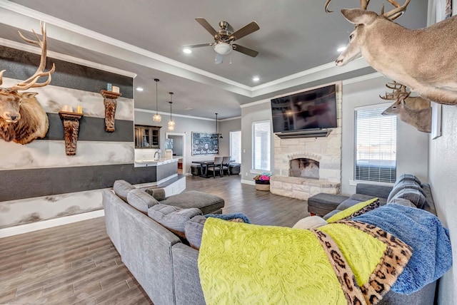 living room featuring wood finished floors, baseboards, a ceiling fan, a fireplace, and a raised ceiling