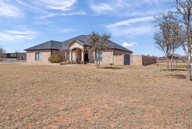 french country inspired facade with stone siding, brick siding, a front lawn, and fence