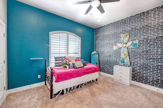 carpeted bedroom with an accent wall, baseboards, brick wall, and ceiling fan