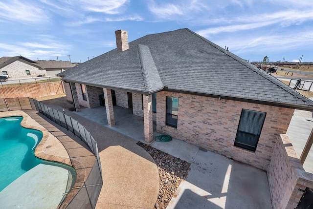 rear view of house featuring a patio, a fenced backyard, a shingled roof, a fenced in pool, and a chimney