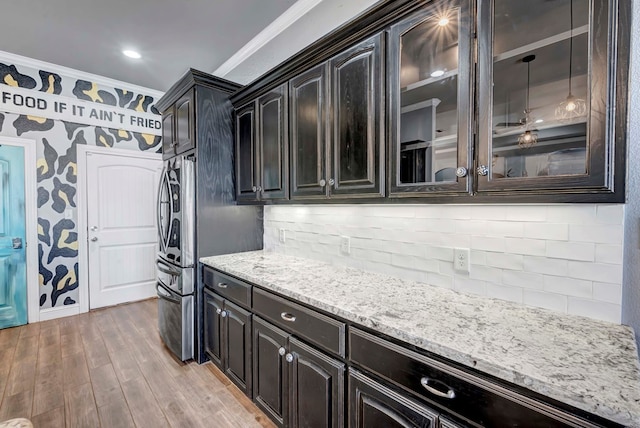 kitchen with light wood-style flooring, tasteful backsplash, crown molding, glass insert cabinets, and light stone countertops