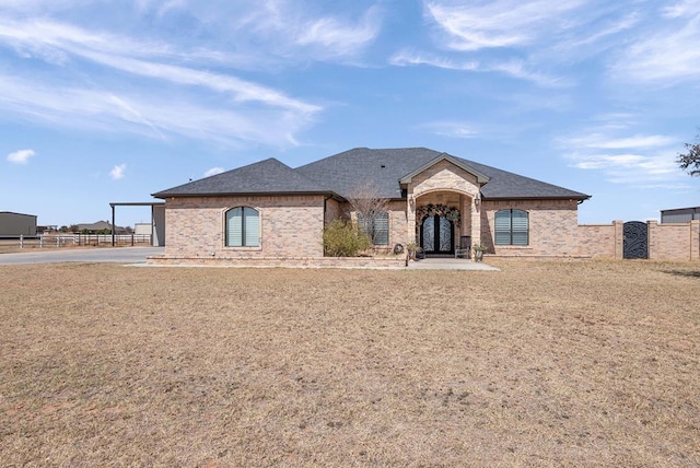 french country style house with brick siding, a shingled roof, and fence