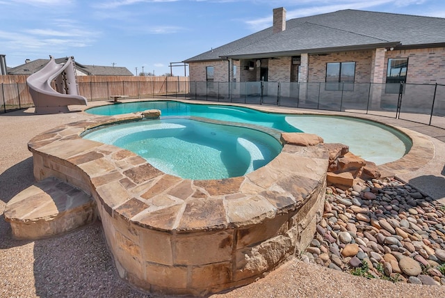 view of swimming pool with a pool with connected hot tub, a water slide, and fence