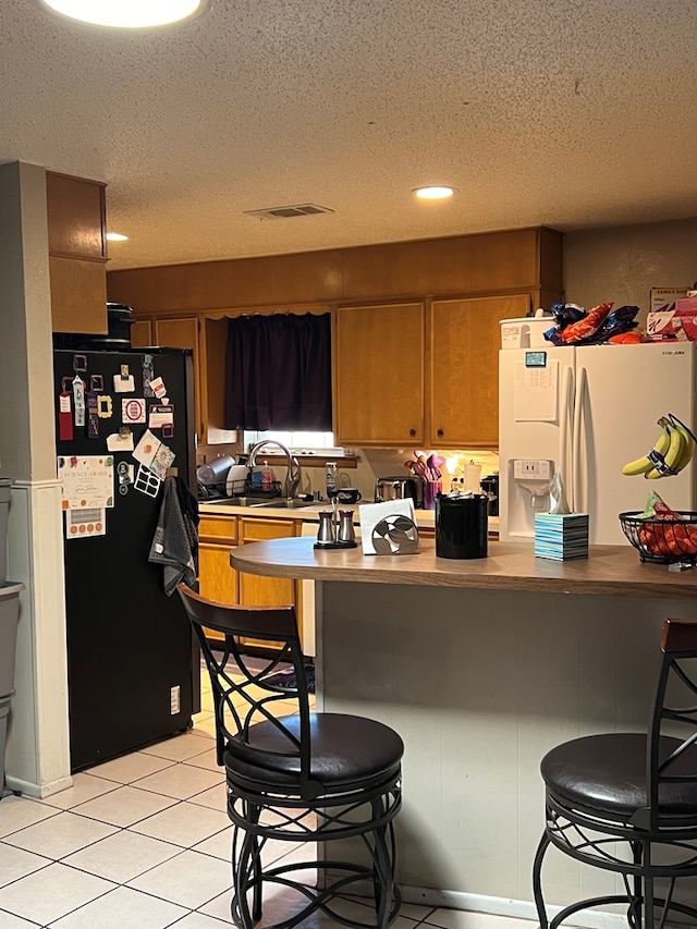 kitchen featuring black refrigerator, a textured ceiling, white fridge with ice dispenser, and a breakfast bar area