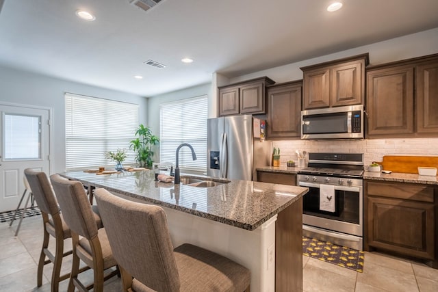 kitchen with visible vents, a sink, stainless steel appliances, dark stone counters, and decorative backsplash