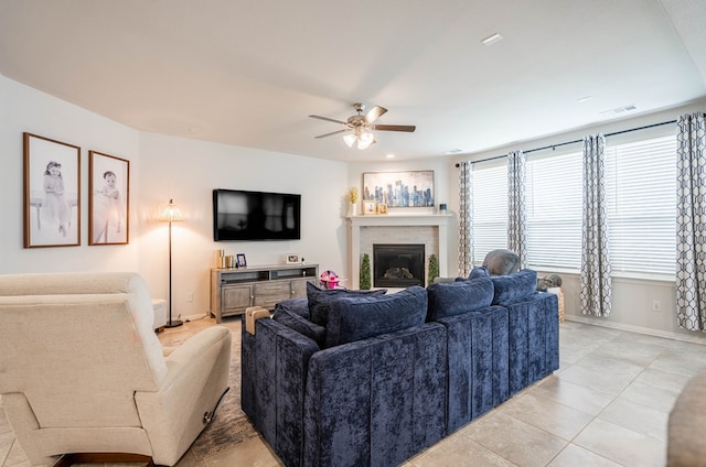 living room with a glass covered fireplace, visible vents, baseboards, and a ceiling fan