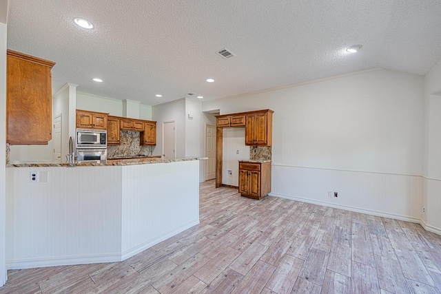 kitchen with light wood-type flooring, appliances with stainless steel finishes, kitchen peninsula, light stone countertops, and backsplash