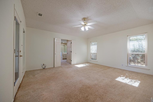 unfurnished bedroom with multiple windows, ceiling fan, light colored carpet, and a textured ceiling