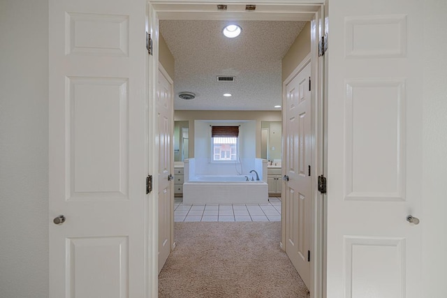 hallway featuring light colored carpet and a textured ceiling