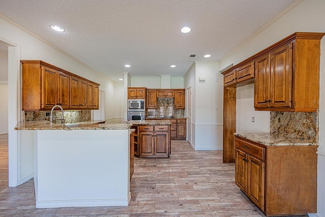 kitchen with appliances with stainless steel finishes, light stone counters, kitchen peninsula, crown molding, and light hardwood / wood-style flooring