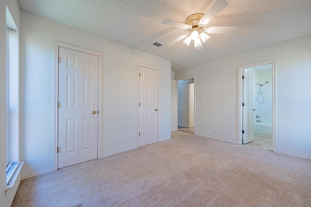 unfurnished bedroom with ceiling fan, light colored carpet, a textured ceiling, and ensuite bath