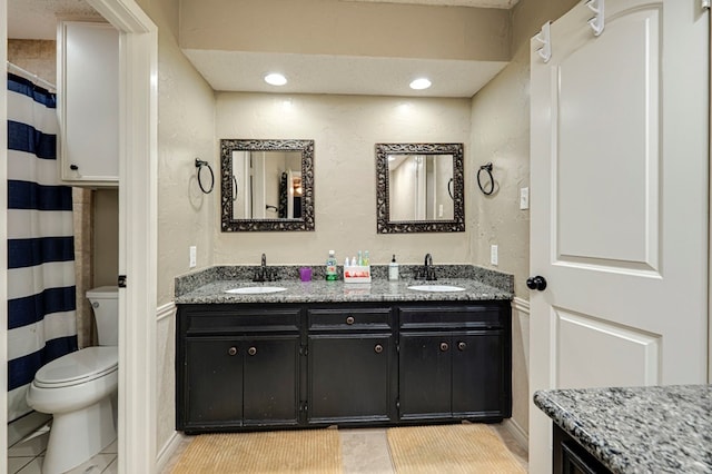 bathroom with double vanity, tile patterned flooring, toilet, and a sink