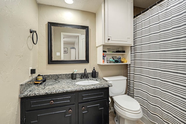 bathroom featuring vanity, toilet, a textured wall, and a textured ceiling