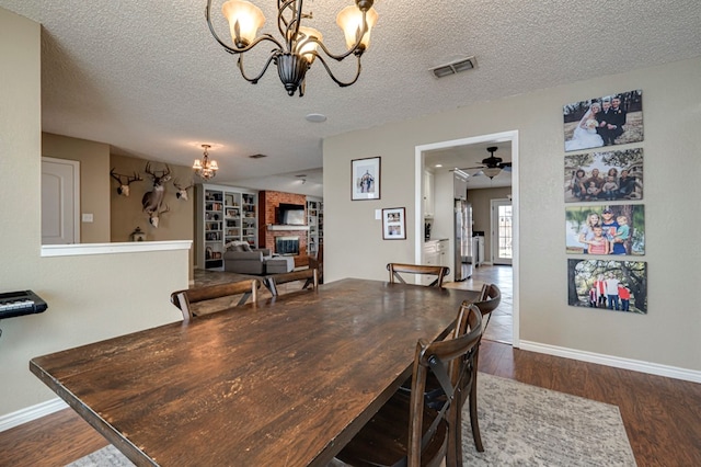 dining room featuring dark wood finished floors, visible vents, a brick fireplace, and a textured ceiling