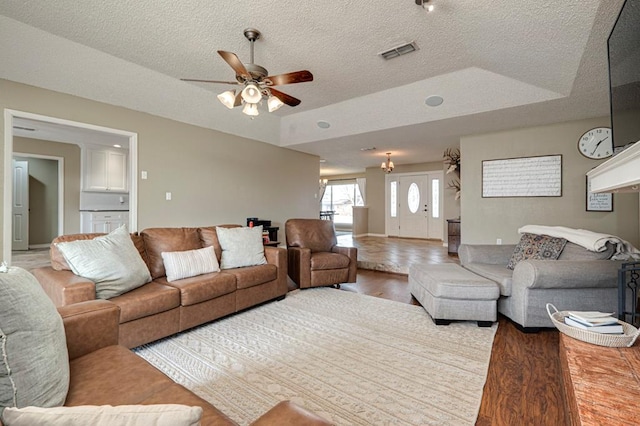 living area with visible vents, a ceiling fan, a textured ceiling, wood finished floors, and a raised ceiling