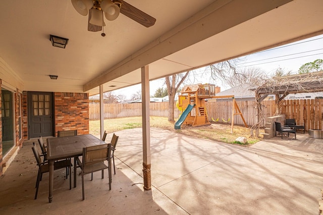 view of patio / terrace featuring a fenced backyard, outdoor dining space, a playground, and a ceiling fan