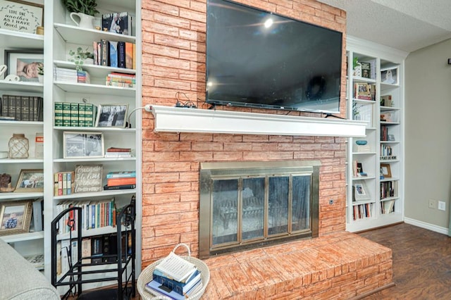 living room with baseboards, a textured ceiling, a brick fireplace, and wood finished floors