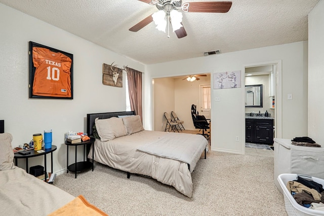 bedroom with a ceiling fan, visible vents, a textured ceiling, light colored carpet, and connected bathroom