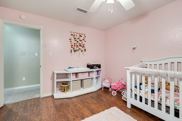 bedroom featuring a ceiling fan, a nursery area, wood finished floors, and visible vents