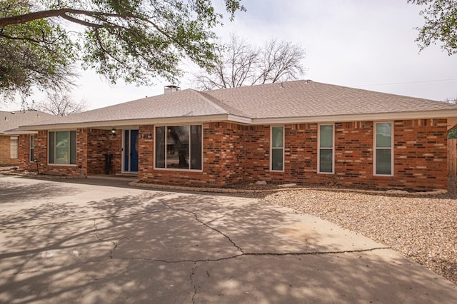 ranch-style house with a shingled roof, brick siding, and a chimney